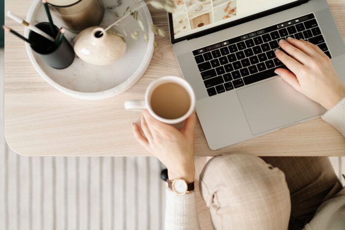 Woman holding a cup of coffee with one hand on her laptop keyboard